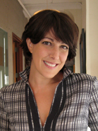 A smiling woman with short dark hair wearing a black and white patterned blouse.