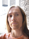 A person with long light brown hair and an orange shirt looking forward.