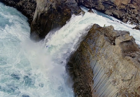 White ocean waves crashing violently against dark, textured rock formations.