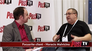 Two men sit facing each other and talk in front of a white wall with red Post TV logos.