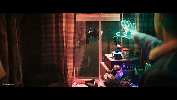 A person's hand reaches toward a window displaying glowing blue holographic elements and various gadgets.