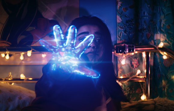 A person reaches toward the camera with a hand emitting a bright, glowing blue light.