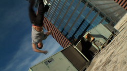 A person mid-flip against a blue sky and tall city buildings.