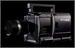 A black professional video camera positioned against a solid black background.