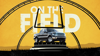 A black pickup truck sits on a pedestal in front of a large goalpost and roller coaster tracks on a yellow background.