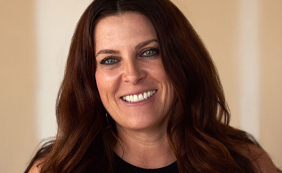 A smiling woman with long, wavy reddish-brown hair looking directly at the camera.