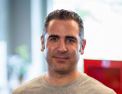 A man with dark, slicked-back hair and a slight smile looking directly at the camera.