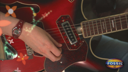 A person's hand strumming the strings of a red electric guitar decorated with floral graphics.