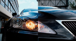 Close-up view of a black car's illuminated headlight and reflective front hood.