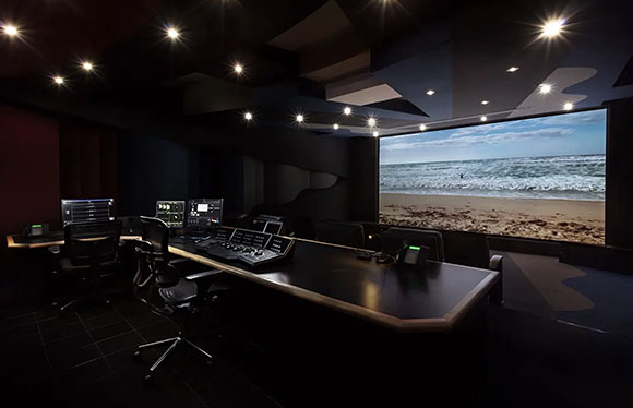 A dark professional editing suite featuring a large screen showing ocean waves and a control console.