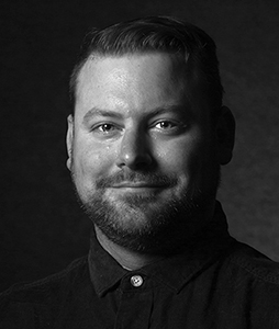Black and white headshot of a man with short hair and a beard, smiling slightly.
