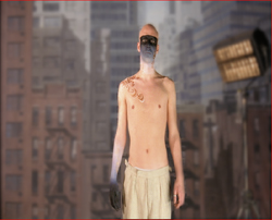 A shirtless man with black face paint and a mask stands before a blurred cityscape.