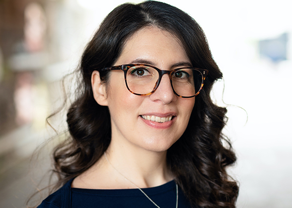 A woman with dark wavy hair and tortoiseshell glasses smiling at the camera.