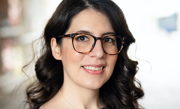 A woman with dark wavy hair and tortoiseshell glasses smiling at the camera.