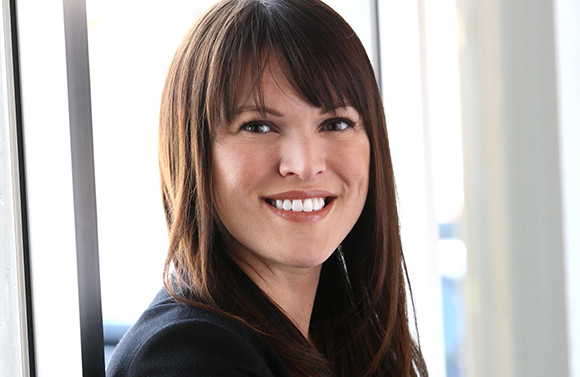 A smiling woman with long brown hair and bangs looking toward the camera.