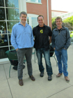 Three men standing together on a patio in front of a building.
