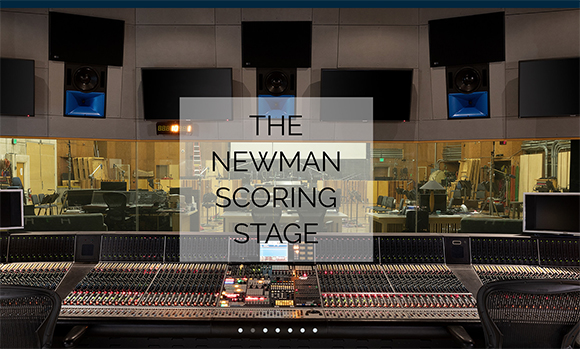 A wide view of a professional recording studio featuring a large mixing console and wall-mounted monitors.