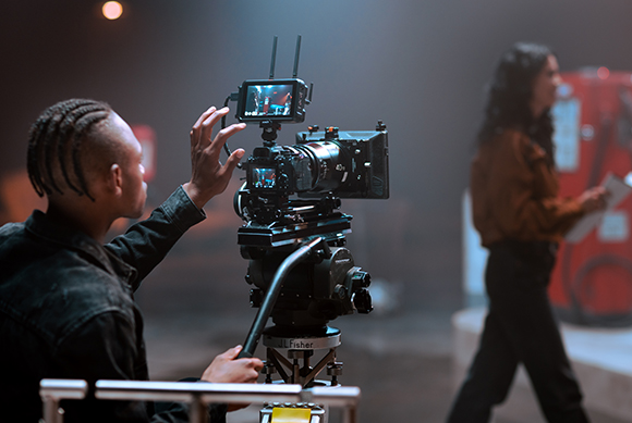 A person adjusts a large professional film camera mounted on a tripod during a production.