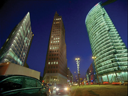 Low angle view of three illuminated skyscrapers against a dark blue night sky.