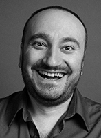 Black and white close-up portrait of a smiling man with a beard and short hair.