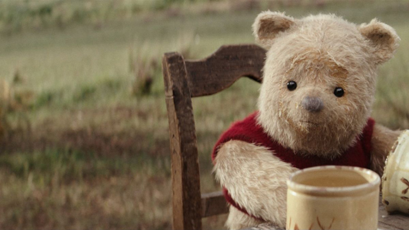 A tan teddy bear wearing a red shirt sits in a wooden chair in a grassy field.