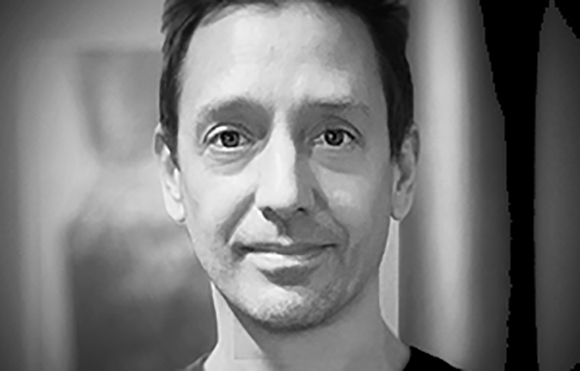 Black and white close-up portrait of a man looking directly at the camera with a slight smile.