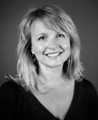 A smiling woman with blonde hair looking toward the camera in a black and white portrait.