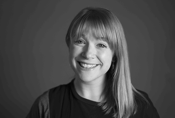 Black and white headshot of a smiling woman with straight hair and bangs.