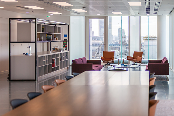 A modern office interior featuring a long wooden conference table and a lounge area with colorful armchairs.