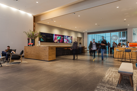 A wide view of a modern building lobby with a long wooden desk and people walking in motion blur.