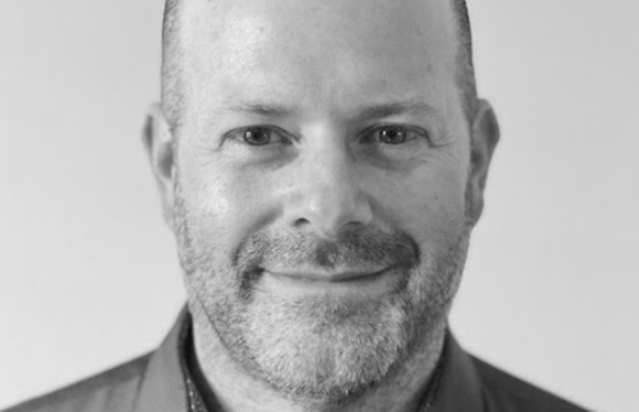 Black and white close-up portrait of a smiling man with short hair and a beard.