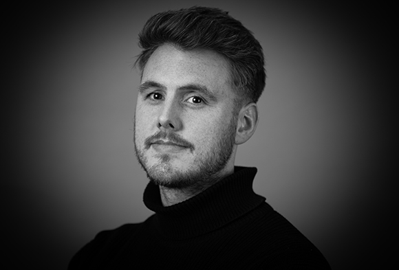 Black and white studio portrait of a man with short hair and a beard wearing a dark turtleneck.