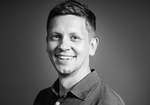A smiling man with short hair looking toward the camera in a black and white headshot.