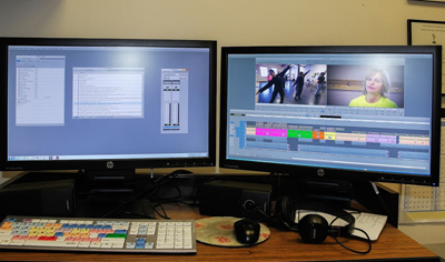 Two computer monitors on a desk showing video editing software, a keyboard, mouse, and headphones.