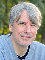Close-up portrait of a middle-aged man with grey hair and light eyes looking at the camera.