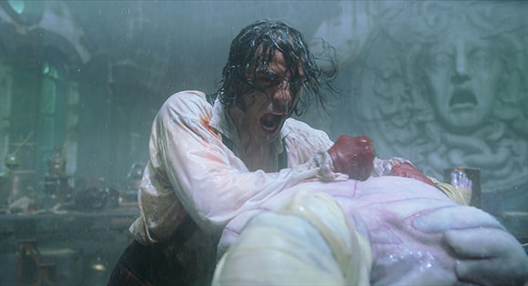 A man with dark, wet hair leans over a pale body in a dimly lit, misty room.