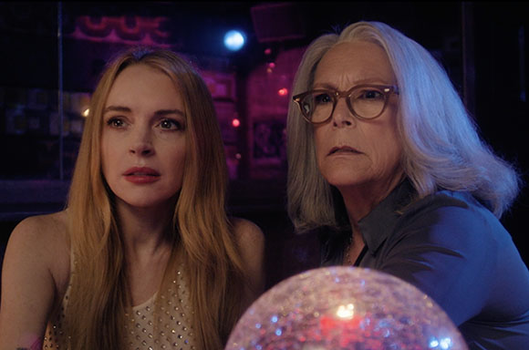 A blonde woman and an older woman with grey hair and glasses look intently at a glowing crystal ball.