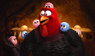 A large red-headed turkey with several small pink and blue chicks perched on its body and nearby.