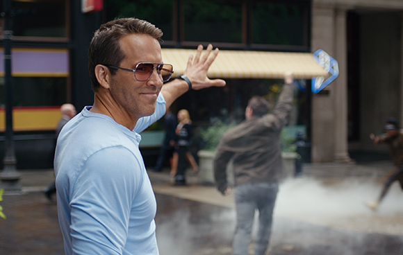 A man in a light blue shirt smiles while holding a long wooden board over his head in a city street.