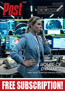 A woman in a blue suit stands in a high-tech control room filled with glowing monitors.