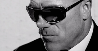 Black and white close-up of a man's face wearing dark sunglasses and a suit.