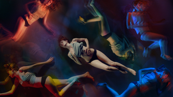 Several figures in swimwear float through a dark space filled with blue, red, and yellow light.