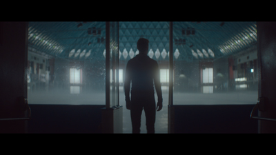 Silhouette of a man standing in a doorway facing a large, misty, brightly lit hall.