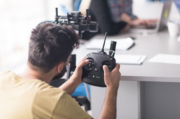 A person's hands holding a black drone remote controller with joysticks and an antenna.