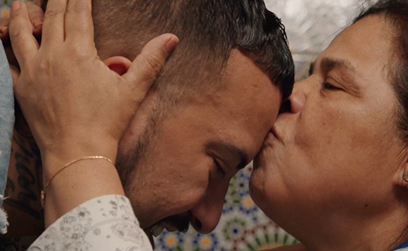 A woman gently holds a man's head and kisses his forehead.