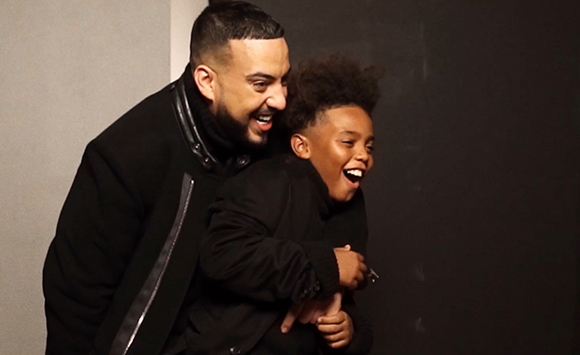 A man in a black jacket smiles and laughs while holding a young boy in a black jacket who is also laughing.