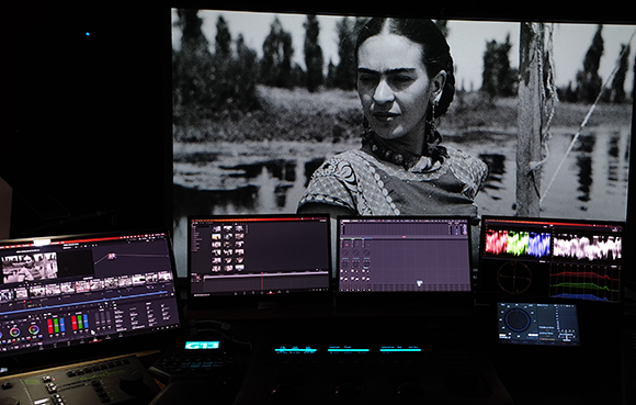 Multiple computer monitors displaying video editing software and a large black and white portrait.
