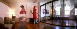 A lounge with armchairs, a large red monster mascot, and a glass-walled meeting room.