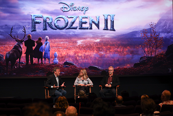 Three panelists sit on a stage before a large Frozen II movie backdrop during a presentation.