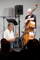 A man plays a double bass while a woman in a white shirt gestures during a live musical performance.